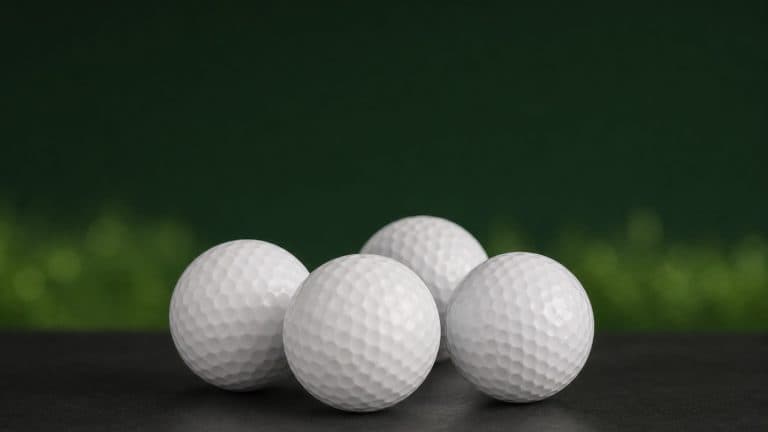 Four plain white golf balls on a dark surface against a deep green background with soft fairway-grass bokeh