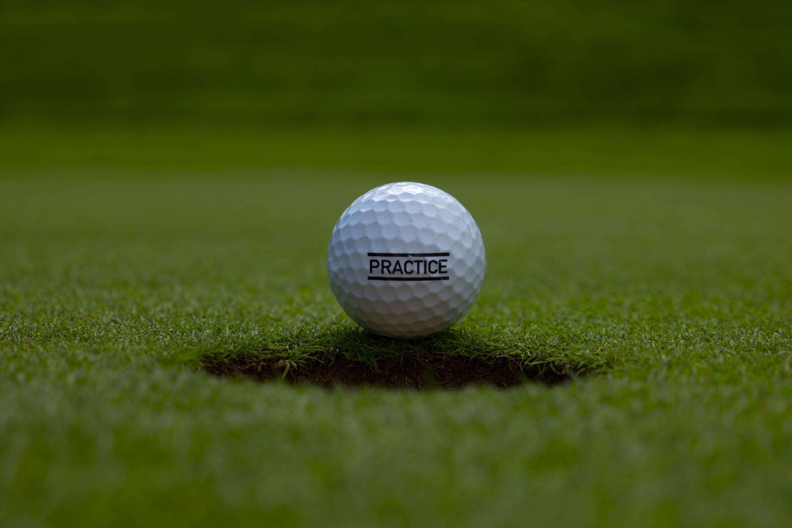 A closeup of a practice text written on a golf ball on the lawn under the sunlight